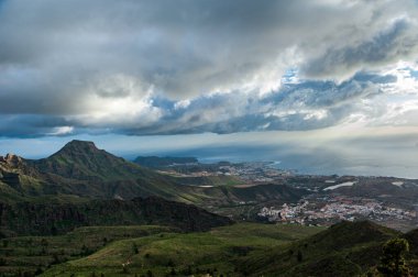 Kanarya Adaları 'nın doğası ve manzarası - dağlar ve Gran Kanaryası' nın doğası. Yeşil dağlar, kıyı köyleri, küçük çam ağaçları ve okyanusun üzerindeki bulutlu gökyüzü. Gran Kanaryası, Kanarya Adaları, İspanya
