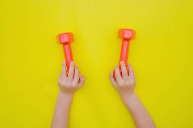 Çocukların elleri sarı arka planda kırmızı halterleri tutar..