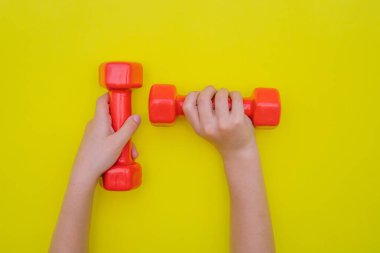 Çocukların elleri sarı arka planda kırmızı halterleri tutar..