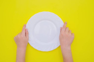 Çocukların elleri sarı arka planda beyaz boş bir tabak tutuyor. Sağlıklı ve düzgün beslenme kavramı.