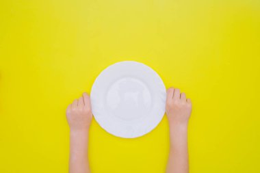 Çocukların elleri sarı arka planda beyaz boş bir tabak tutuyor. Sağlıklı ve düzgün beslenme kavramı.