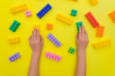 Çocuk elleri, inşaatçının detaylarını sarı arka planda tutar. Çok renkli inşaat blokları. Çocukların eğitici oyunu. Arkaplan ve doku.