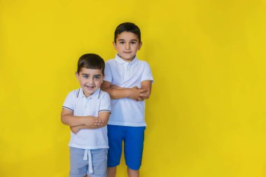 Küçük çocuklar sarı bir zeminde otururlar. Kardeşler ya da arkadaşlar gülümser ve eğlenirler. Anaokulu çağındaki çocuklar.