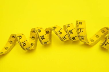 Sarı arka planda sarı renkli santimetre şeridi. Mesafeleri ölçmek için bir araç. Dikiş ve dikiş için santimetre.