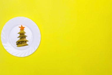 Beyaz bir tabak turşu ve noel ağacı şeklinde bezelye üzerinde. Havuç yıldızı. Masanın dekorasyonu. Yeni yılın atmosferi..