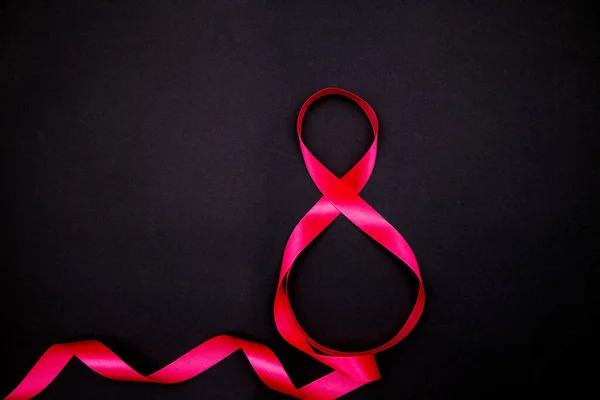On a black background, a pink satin ribbon in the form of the number eight. Gift wrap. — Stock Photo, Image