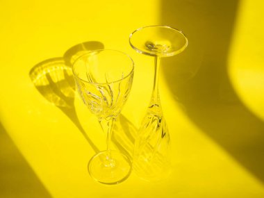 Boş bardaklar sarı bir arkaplanda duruyor. Sert gölgeler ve camlardan yansıyan parlak ışıklarla dolu güzel, yaratıcı bir hayat. Güneş ışığı camlara çarpıyor..