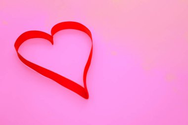 Pembe arka planda, kalp şeklinde pembe saten bir kurdele. Hediye paketi. 8 Mart ve Sevgililer Günü konsepti.