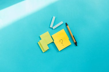 Farklı boyutlarda ve renklerde çıkartmalar mavi arka plana yerleştirilir. Yanında bir kalem var..