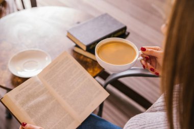 Genç bir kız bir kafede oturuyor ve bir kitap okuyor. Kız kahve ya da kakao içiyor. Sıcak atmosfer ve keyifli zaman. Dinlenme ve rahatlama..