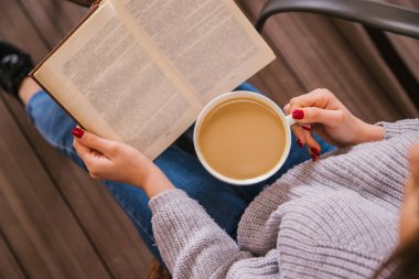 Genç bir kız bir kafede oturuyor ve bir kitap okuyor. Kız kahve ya da kakao içiyor. Sıcak atmosfer ve keyifli zaman. Dinlenme ve rahatlama..