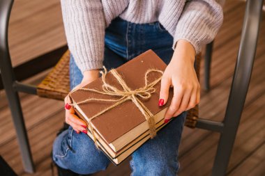 Genç bayanın kucağında bir yığın kitap var. Kitaplar iple bağlanmış. Kız kazak ve kot pantolon giyiyor. Öğrenci ve okul çocuğu. Kütüphaneden kitaplar. Ders kitaplarını yakından çek..