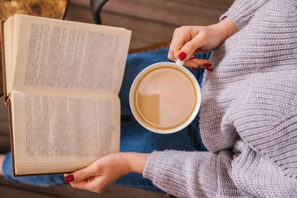 Genç bir kız bir kafede oturuyor ve bir kitap okuyor. Kız kahve ya da kakao içiyor. Sıcak atmosfer ve keyifli zaman. Dinlenme ve rahatlama..