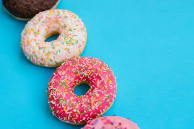 Farklı renklerde tatlı çörekler mavi arka planda sıralanır. Şekerleme ürünleri. Zararlı fast food. Parlak renkli arka plan..