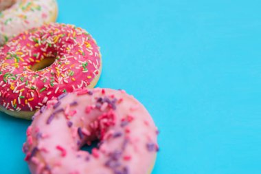 Farklı renklerde tatlı çörekler mavi arka planda sıralanır. Şekerleme ürünleri. Zararlı fast food. Parlak renkli arka plan..