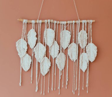 Macrame kahverengi bir duvarda asılı. Püsküller yakın planda beyazdır. İç kısım elle yapılmıştır. İpliklerin ve dokuların dokusu. Odanın iç dekorasyonu..