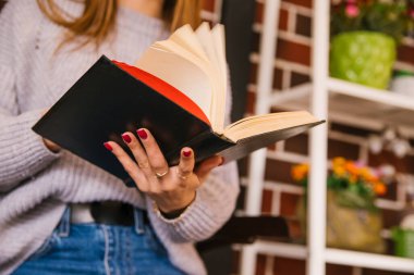 Gri örgü kazaklı güzel bir kız rahat bir kafede kitap okuyor. Keyifli vakit geçirme ve iletişim kavramı. Öğrenci ya da iş kadını.
