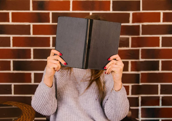 The young woman covered her face with a hardcover book. The cover is black. A photo without a face.