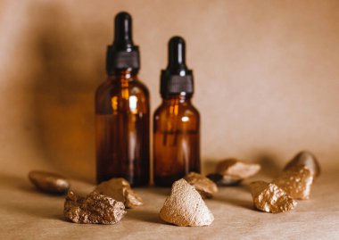 Taşların arasında pipetli bir kaptaki kozmetik yağı duruyor. Aromaterapi için gerekli yağ. Bej, kompozisyonun doğal rengidir ve taşlar altın rengidir..