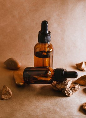 Taşların arasında pipetli bir kaptaki kozmetik yağı duruyor. Aromaterapi için gerekli yağ. Bej, kompozisyonun doğal rengidir ve taşlar altın rengidir..