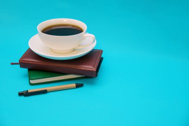 İki deri kaplı defter mavi arka planda üst üste yatar. Üstte bir fincan kahve var. İş ve eğitim konusu..