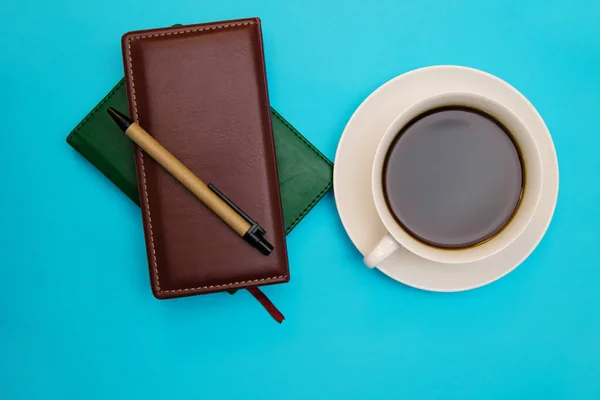 Two leather-bound notebooks lie against a blue background. There\'s a pen and a cup of coffee next to it. Top view. The topic of business and training.