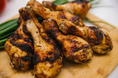 Kızarmış tavuk bacağı tahta bir tahtanın üzerinde yatıyor. Yanında sebze ve yeşil soğan olan tavuk şiş kebap. Yaz et yemeği.