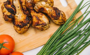 Kızarmış tavuk bacağı tahta bir tahtanın üzerinde yatıyor. Yanında sebze ve yeşil soğan olan tavuk şiş kebap. Yaz et yemeği.