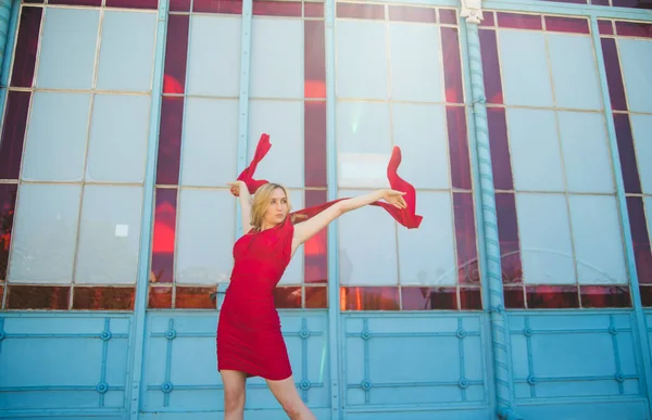 A young woman stands against a stained-glass wall and is wearing a red dress. The fabric of the dress flies beautifully in the air. The atmosphere of freedom in the photo.