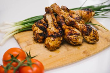 Kızarmış tavuk bacağı tahta bir tahtanın üzerinde yatıyor. Yanında sebze ve yeşil soğan olan tavuk şiş kebap. Yaz et yemeği.