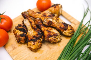 Kızarmış tavuk bacağı tahta bir tahtanın üzerinde yatıyor. Yanında sebze ve yeşil soğan olan tavuk şiş kebap. Yaz et yemeği.