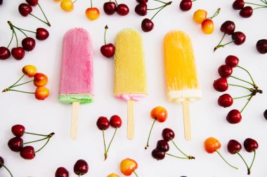 Beyaz arka planda kirazların arasında üç farklı renkte dondurma var. Kirazlar sarı ve koyu kırmızıdır. Yaz ferahlatıcı tatlı.