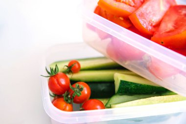 Beyaz arka planda plastik kaplarda kesilmiş sebzeler. Salatalık ve domates kabın içinde. Sağlıklı ve düzgün beslenme. İş ya da seyahat için öğle yemeği..