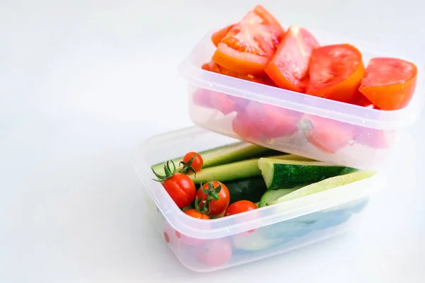 Beyaz arka planda plastik kaplarda kesilmiş sebzeler. Salatalık ve domates kabın içinde. Sağlıklı ve düzgün beslenme. İş ya da seyahat için öğle yemeği..