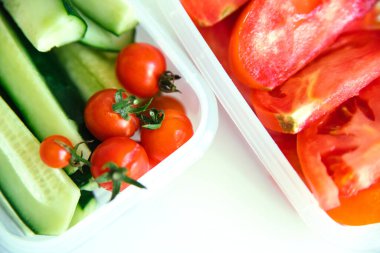 Beyaz arka planda plastik kaplarda kesilmiş sebzeler. Salatalık ve domates kabın içinde. Sağlıklı ve düzgün beslenme. İş ya da seyahat için öğle yemeği..