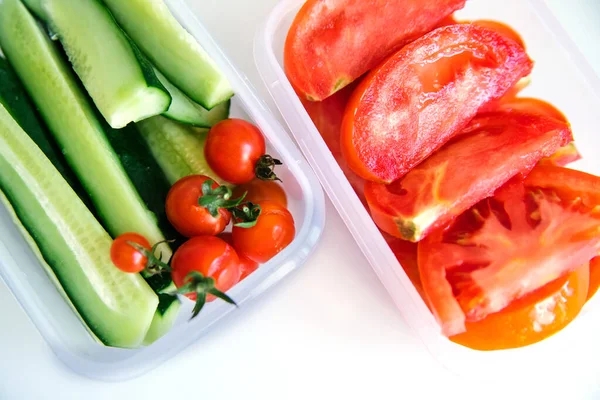 Beyaz arka planda plastik kaplarda kesilmiş sebzeler. Salatalık ve domates kabın içinde. Sağlıklı ve düzgün beslenme. İş ya da seyahat için öğle yemeği..