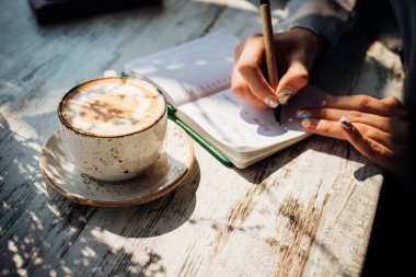 Genç bir kadın pencerenin yanındaki masada oturuyor ve bir deftere yazı yazıyor. Güneş ışınları ve gölgeler masaya düşer. Bir iş kadını bir kafede bağımsız olarak çalışır..