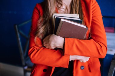 Genç bir kadın bir yığın kitap tutuyor. Mavi duvara karşı kırmızı, modaya uygun ceketli bir kız. Bir öğrenciye ders kitaplarına göre öğretmek. Bir kafede hoş vakit geçirmek..