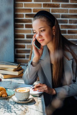 Genç ve güzel bir kadın bir kafede arkadaşlarıyla ya da iş arkadaşlarıyla cep telefonunda konuşuyor. Genç iş adamları kavramı. Kız bilgileri bir deftere yazıyor..