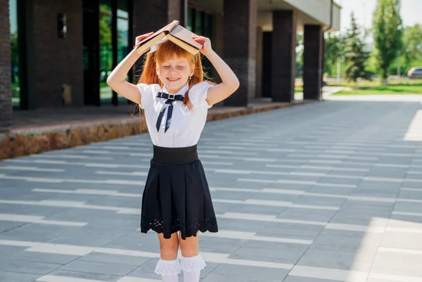 在学校或幼儿园的第一天 一个头戴一本书的有趣迷人的小女孩 一个孩子在外面一个温暖的阳光灿烂的日子里 这个概念又回到了学校 — 图库照片