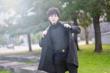 Modaya uygun bir milenyum modeli paltosunu yumuşak bir sonbahar parkında ayarlıyor.