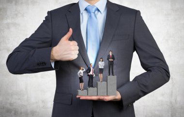 A man holding a pedestal in the shape of a bar chart, four businesspeople standing on it. Front view, no head. Concrete background. Concept of career growth.