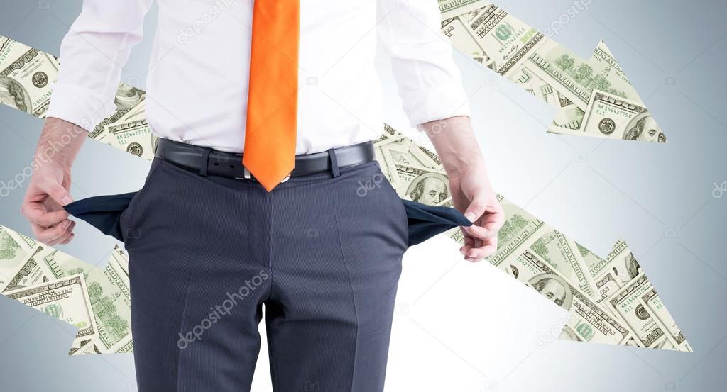 A businessman with an orange tie turning his empty pockets inside out. Front view, no head. Dollar arrows at the grey background. Concept of bankruptcy.