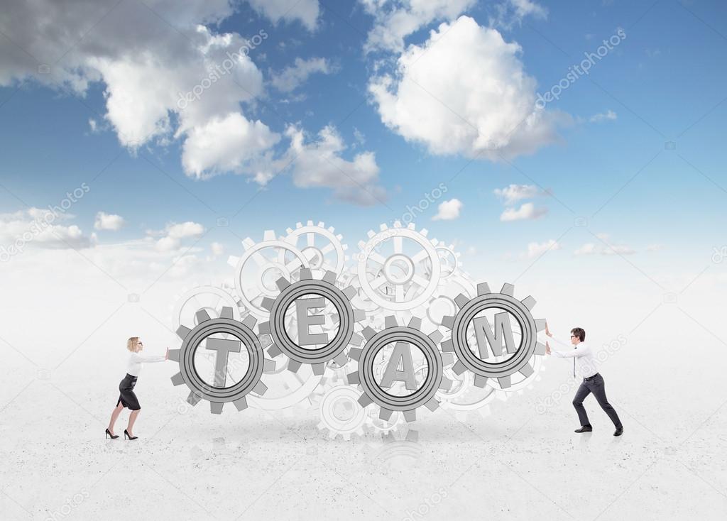 A businesswoman and a businessman pushing cogwheels with letters t, e, a, m to each other. Blue sky at the background.