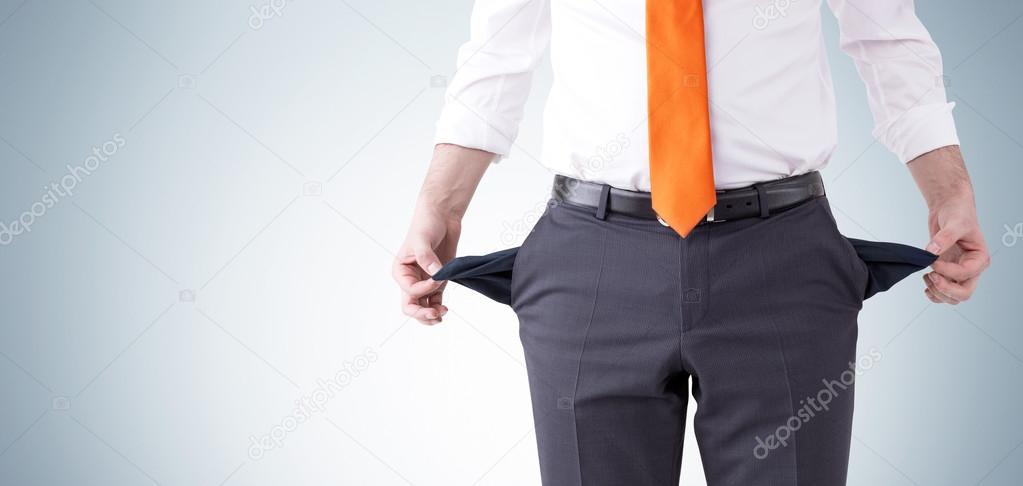A businessman with an orange tie turning his empty pockets inside out. Front view, no head. Grey background. Concept of bankruptcy.