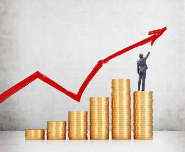Businessman on pile of coins painting red graph.