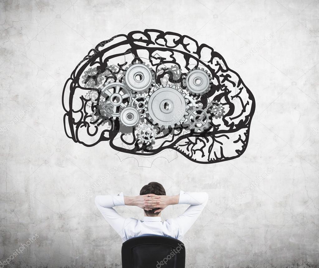 Businessman sitting on chair with hands on head and looking at image of brain with gears on concrete wall.