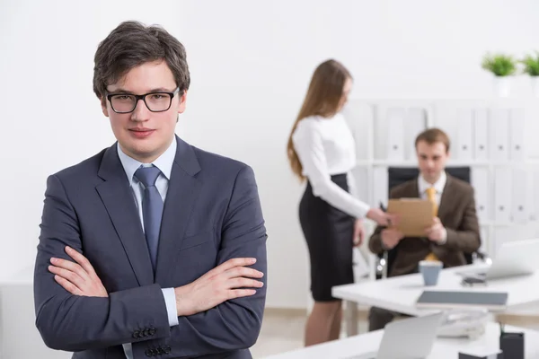 Joven hombre de negocios con las manos cruzadas, dos colegas de fondo. Concepto de trabajo en equipo . — Foto de Stock