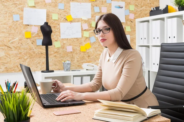 Mulher de óculos trabalhando no computador, alfaiate manequim no fundo . — Fotografia de Stock