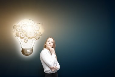 İş kadını yukarı bakıyor, vitesleri bir kenara boyanmış ampul. Ön görüş. Koyu mavi arka plan. Yeni fikir kavramı.